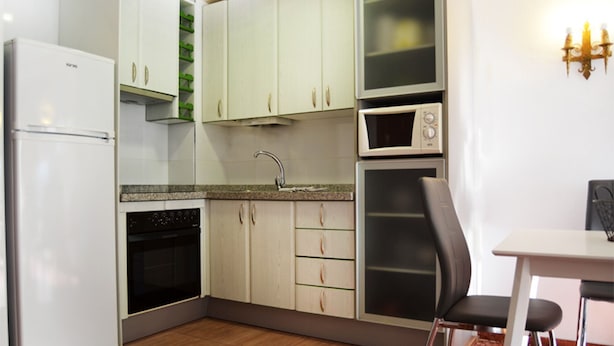 A compact kitchen with a refrigerator, oven, microwave, and a dining area with a chair. - Terrasol Isis G in Caleta de Velez (Velez-Malaga)