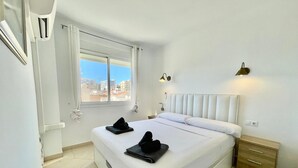 Une chambre d’hôtel avec un grand lit, une fenêtre avec des rideaux, une table de chevet et une petite table de nuit.