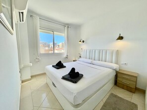 Ein Hotelzimmer mit einem großen Bett, einem Fenster mit Vorhängen, einem Nachttisch und einem Beistelltisch.