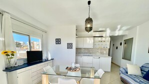 Une cuisine moderne avec des meubles blancs, une table à manger en verre et un canapé recouvert d’un tissu à motifs.