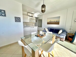 Ein moderner Wohnraum mit einem Glastisch, weißen Stühlen, einem gestreiften Sofa und einer Küchenzeile.