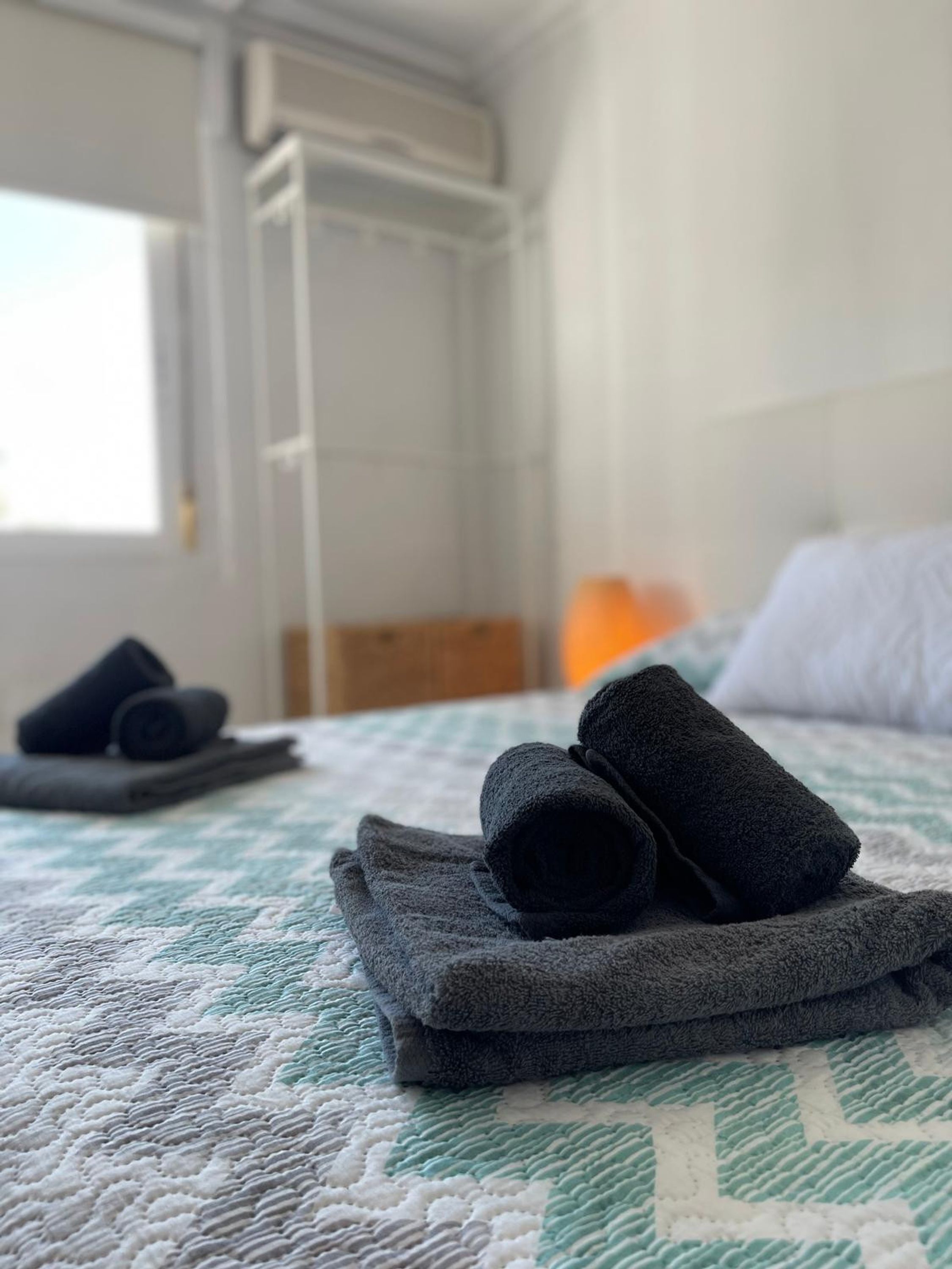 A bed with a quilted bedspread, a folded towel, and a rolled-up towel on it.