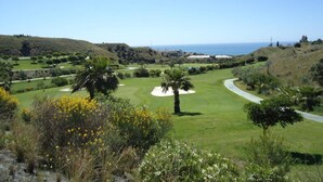 A golf course with a clear view of the ocean, surrounded by hills and greenery. - Terrasol Tico Baviera Golf LAS Carmelitas (Velez-Malaga)