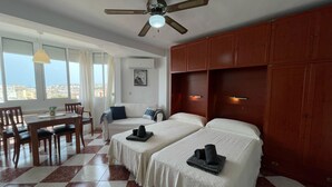 A hotel room with two beds, a dining table, chairs, a ceiling fan, and a view of the city. - Terrasol Plazamar 4-9 (Velez-Malaga)
