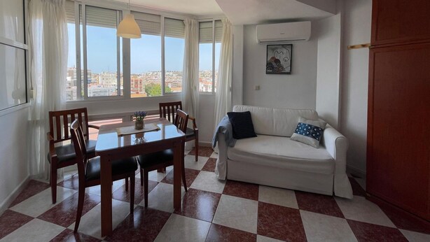 A room with a dining table, chairs, a sofa, a window with curtains, and an air conditioning unit. - Terrasol Plazamar 4-9 (Velez-Malaga)
