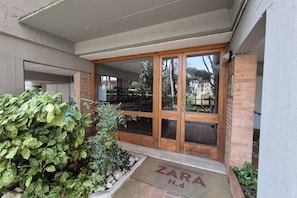 A building entrance with a wooden door, a doormat, and a small garden area. - Located in one of Viareggio’s most desirable areas, just a few steps from the Pineta di Ponente and approximately a 10-minute walk from the beach, the apartment is an ideal choice for those seeking tranquility and comfort in a well-serviced residential (Viareggio)