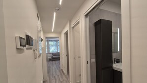A modern hallway with a light wood floor, white walls, and a dark-toned bathroom with a sink and mirror. - Located in one of Viareggio’s most desirable areas, just a few steps from the Pineta di Ponente and approximately a 10-minute walk from the beach, the apartment is an ideal choice for those seeking tranquility and comfort in a well-serviced residential (Viareggio)