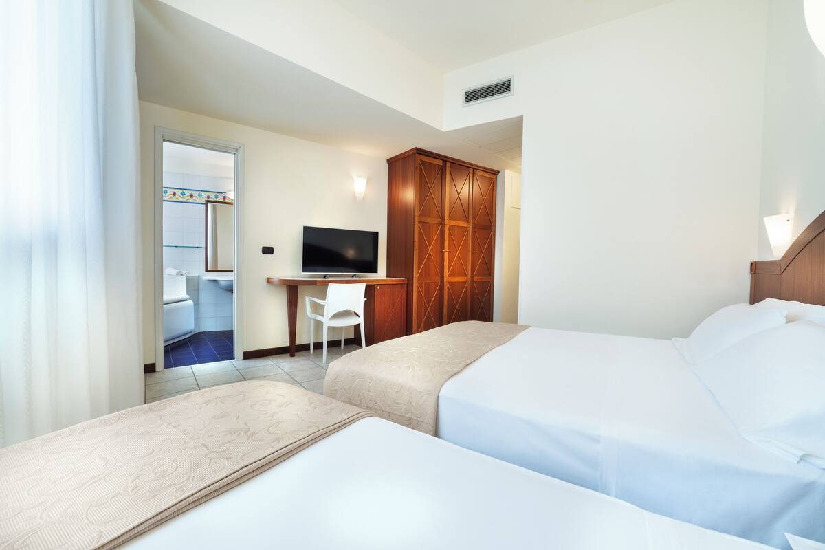 A hotel room with two beds, a desk with a chair, a television, and a wardrobe.