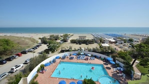Zona de piscina con vista a la playa, sillas de descanso y sombrillas.