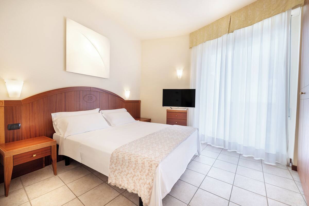A hotel room with a bed, bedside table, TV, and curtains.