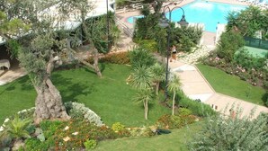 Un jardín ajardinado con piscina, un árbol grande y un farol.