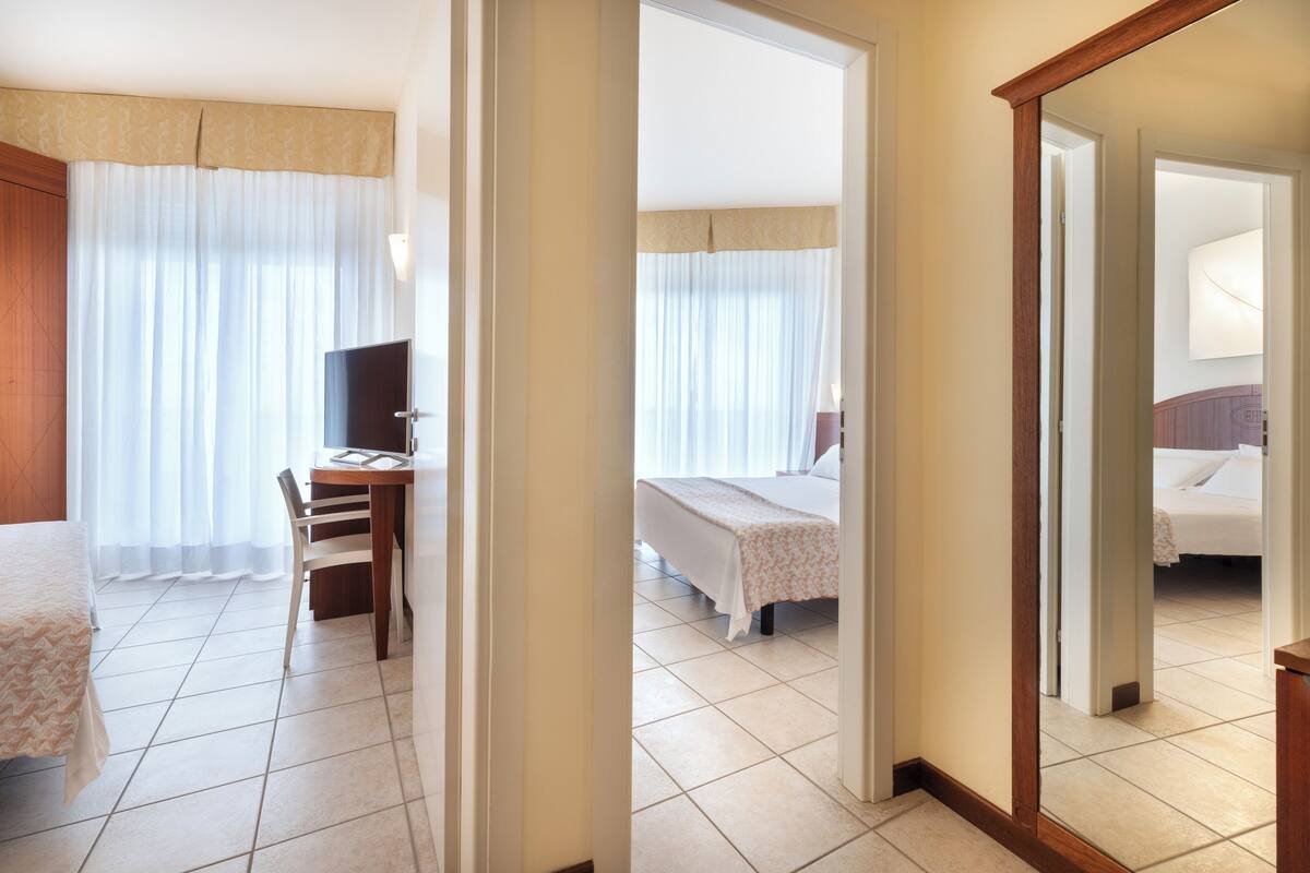 A hotel room with a bed, a desk with a chair, a television, and a bathroom visible through an open door.