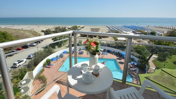 Un balcón con mesa dispuesta para el té, una piscina y vista a la playa.
