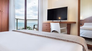 Habitación de hotel con cama, escritorio con televisor, una silla y vista al mar.