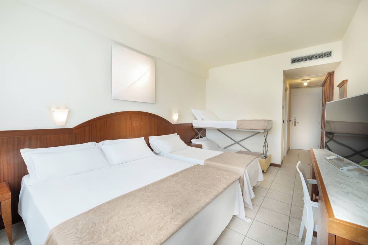 A hotel room with two beds, a desk, and a TV.