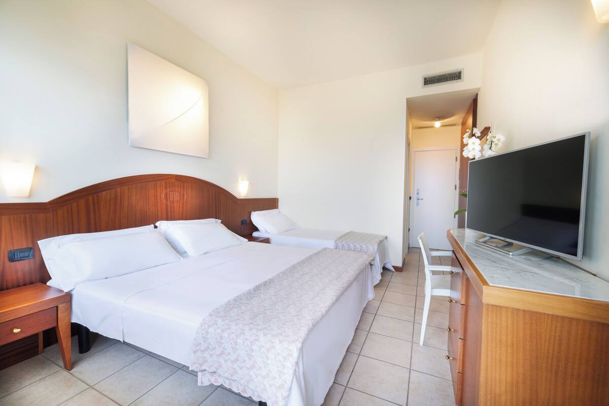 A hotel room with two beds, a TV, a desk, and a bathroom visible through an open door.