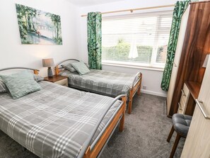 Une chambre avec deux lits, une table de chevet, une lampe, une fenêtre avec des rideaux et un bureau avec une chaise.