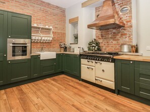 A kitchen with green cabinets, a brick wall, a wooden floor, a stove, and a sink. - Milton Manor, Milton On Stour (Gillingham)