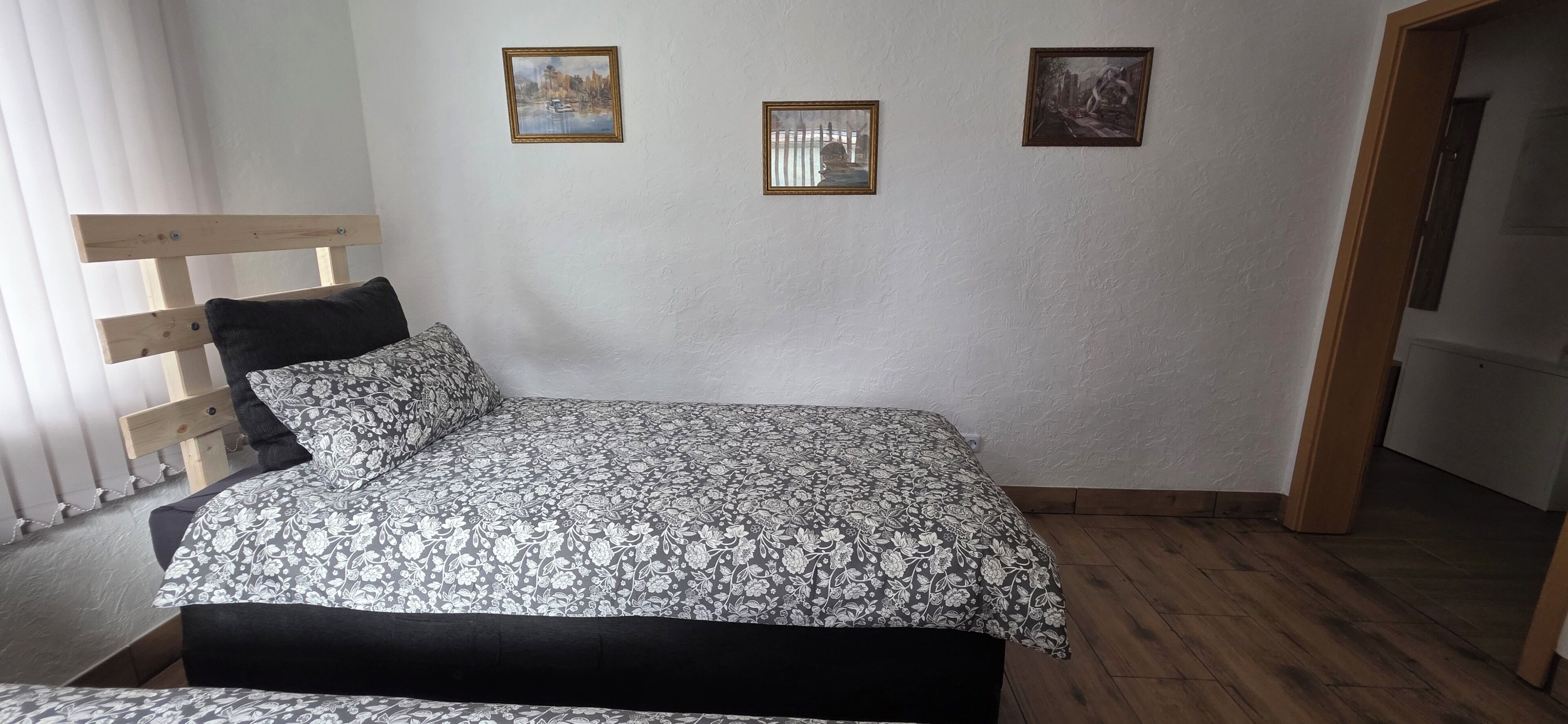 Un dormitorio con una cama, dos almohadas, un cabecero de madera y tres cuadros en la pared.