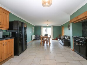 Une cuisine comprenant une table à manger, des chaises, un réfrigérateur, un four et un canapé, le tout dans une pièce aux murs verts.