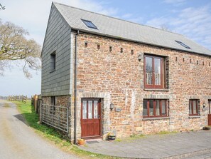 A stone building with a sloped roof, two windows with shutters, and a door.