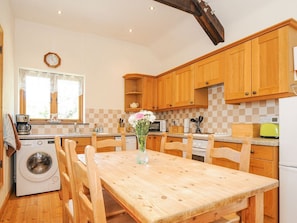 A kitchen with wooden cabinets, a washing machine, a dining table with chairs, and a clock on the wall.