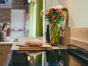 Una encimera de cocina con una hogaza de pan, un cuchillo y un jarrón con flores.