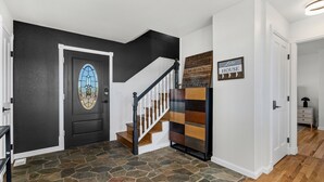 A staircase with a wooden handrail and white balusters, a black door with a stained glass window, and a wall with a 'Like House' sign. - The Lake House on Boyd Private Boat Ramp & Dock (Loveland)