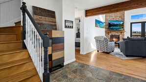 A staircase with wooden steps and a black railing, a living room with a fireplace, a stone wall, and a view of a lake through a window. - The Lake House on Boyd Private Boat Ramp & Dock (Loveland)