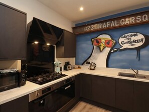 A kitchen with a microwave, toaster, kettle, and a wall mural with a bird and a speech bubble.