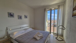Ein modernes Schlafzimmer mit Bett, Nachttisch, einem Fenster mit Vorhängen und Blick auf Gebäude.
