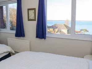 Une chambre avec deux lits, une fenêtre avec des rideaux, un radiateur et un tableau encadré au mur.