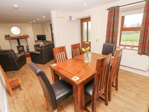 A dining area with a wooden table and chairs, a sofa, a TV, and a fireplace. - Gwynfa, Newcastle Emlyn (Newcastle Emlyn)