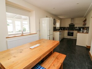Una cocina con una mesa de madera, un refrigerador, un microondas y una ventana con persianas.
