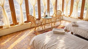 Een kamer met twee bedden, een ronde tafel en stoelen, grote ramen en een houten vloer.