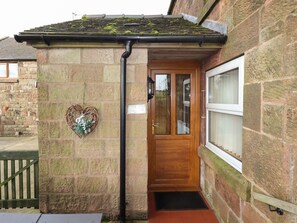 A stone-built house with a wooden door, a heart-shaped decoration, and a window.