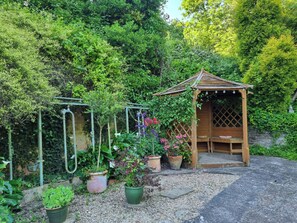 A garden with a wooden gazebo, potted plants, and a metal trellis.