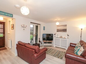 A living room with two brown leather sofas, a television on a white stand, a white cabinet, and a door leading outside. - Herons Reach, Whitby (Whitby)