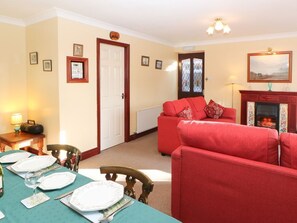 Een woonkamer met een rode bank, een eettafel gedekt voor vier personen, een open haard en een deur met ruit.
