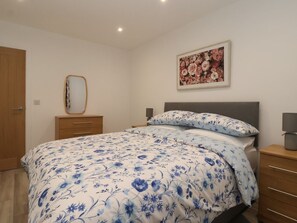 Un dormitorio con cama, cómoda, mesita de noche, espejo y un cuadro con motivos florales en la pared.