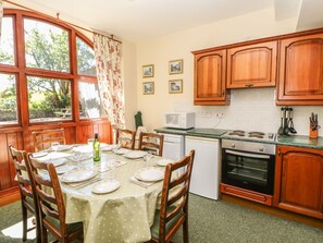 A kitchen with wooden cabinets, a dining table set for four, a microwave, and an oven. - Westfield Cottage, Mickleton, Teesdale (Barnard Castle)