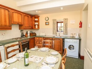 A kitchen with wooden cabinets, a washing machine, and a dining table set for four. - Westfield Cottage, Mickleton, Teesdale (Barnard Castle)