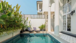 Una piscina con pavimento piastrellato, due sdraio e piante in vaso.