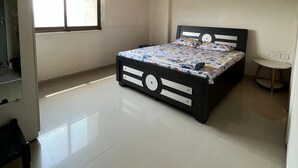 Quarto com cama, ventilador de teto, janela com persianas, mesa de cabeceira e pequena escrivaninha.