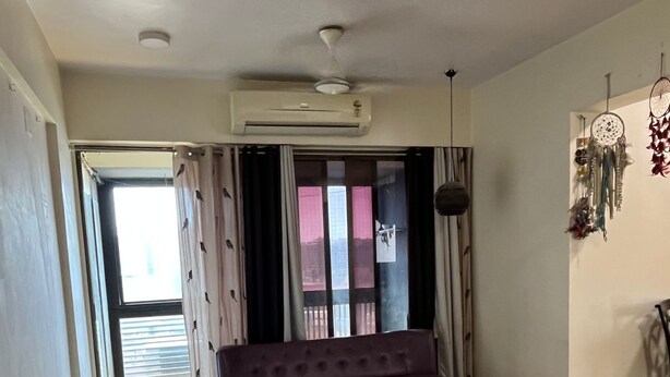 Quarto com escrivaninha, cadeira, sofá roxo, poltrona de espuma e um apanhador de sonhos na parede.
