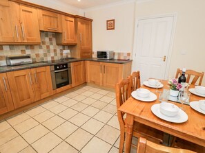 Une cuisine avec des meubles de rangement en bois, un four à micro-ondes et une table à manger pour quatre personnes.