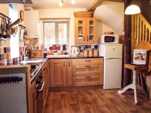 A kitchen with wooden cabinets, a microwave, a refrigerator, and a window with blinds.