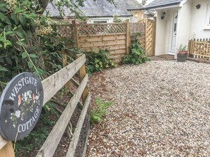 Un camino de grava que conduce a una puerta de madera con un cartel que dice 'Westgate Cottage'.