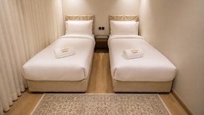 Habitación de hotel con dos camas, piso de madera, alfombra estampada y ventana con cortinas.