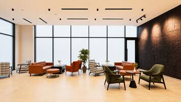A modern lounge area with sofas, armchairs, and a coffee table, featuring large windows and a decorative wall.